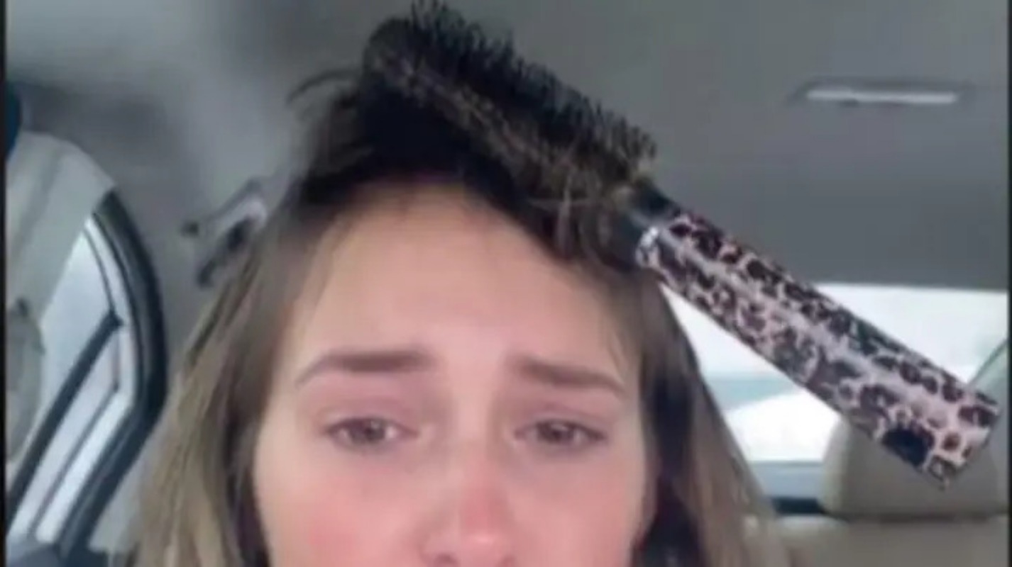 A tentativa de modelagem do cabelo de uma mulher a deixa com uma escova presa na cabeça